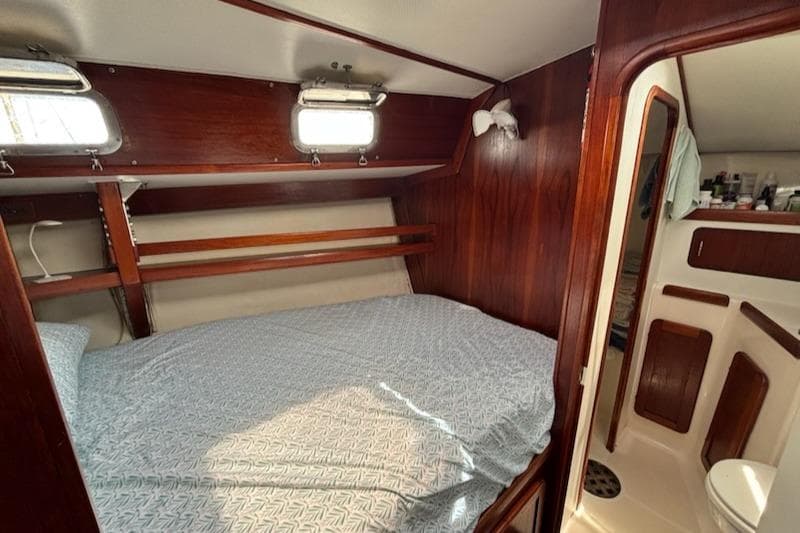 1989 Caliber 38 sailboat cabin with bed, wooden interior, and adjacent bathroom.