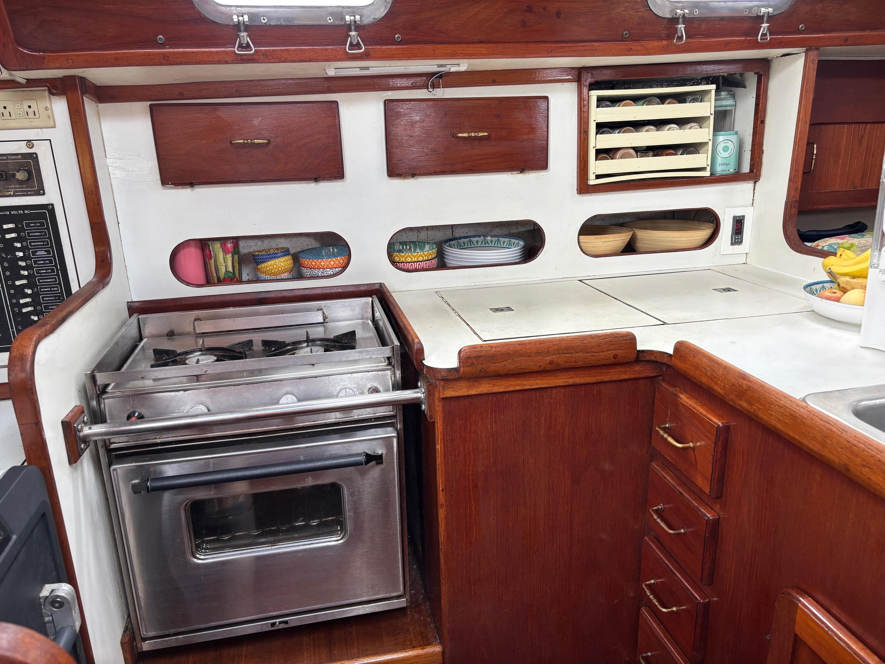 1989 Caliber 38 yacht kitchen with stove, wooden cabinets, and organized dish storage.