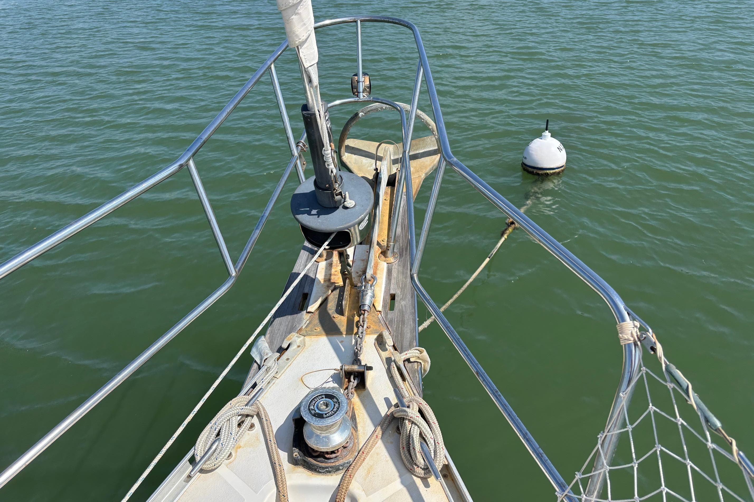 Bow of 1989 Caliber 38 sailboat with anchor and buoy in calm water.