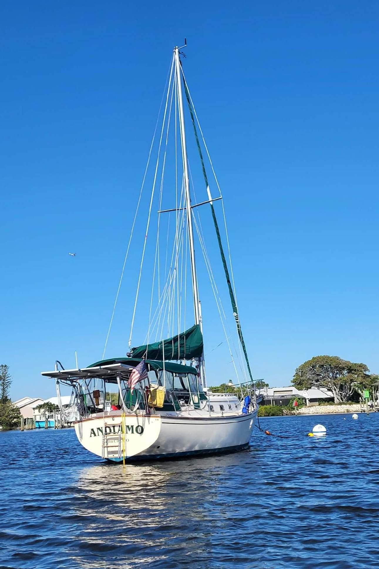 1990 Island Packet 32 sailboat named "Andiamo" on calm water under clear blue sky.