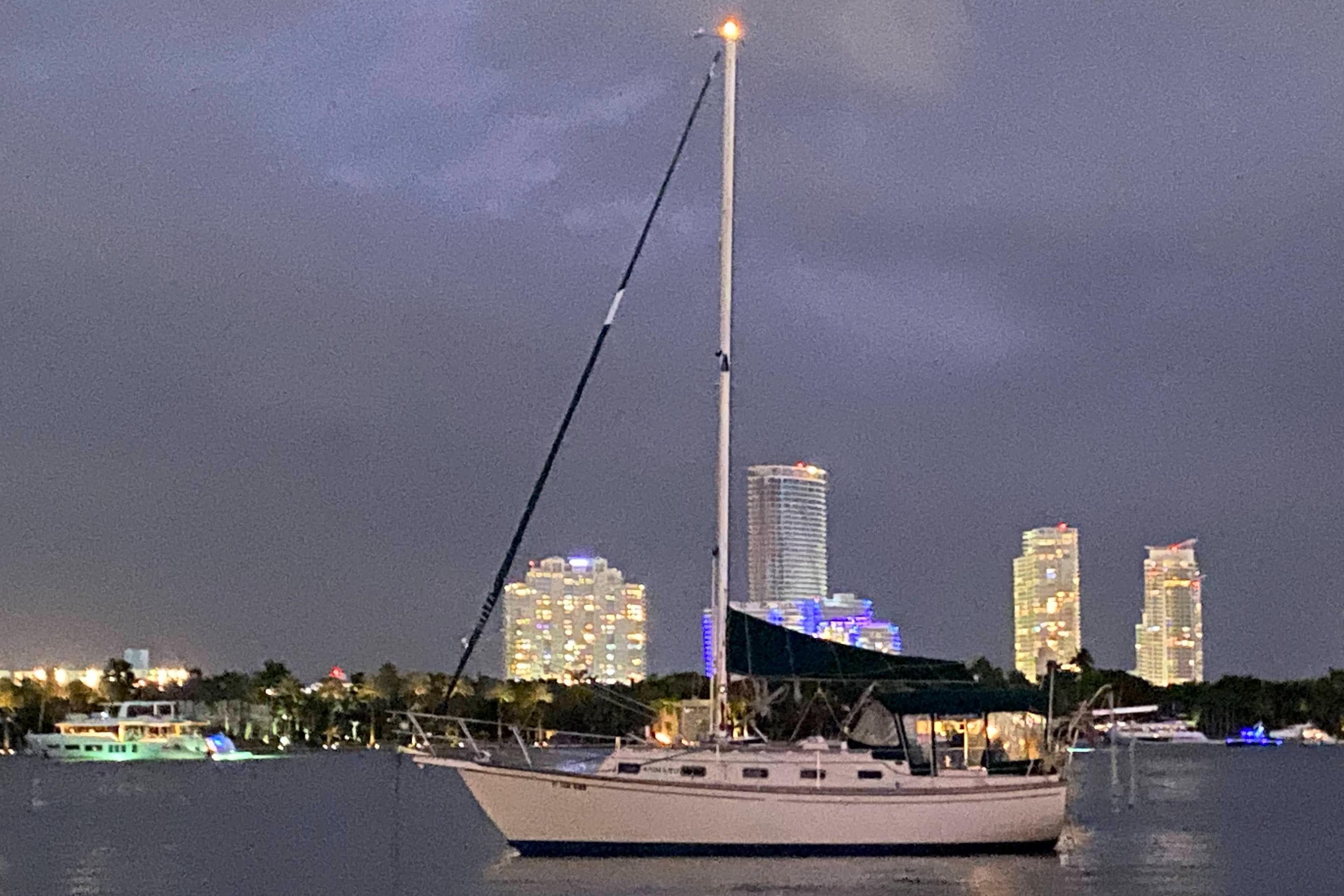 Sailboat Island Packet 32, 1990, anchored at night with city skyline in background.