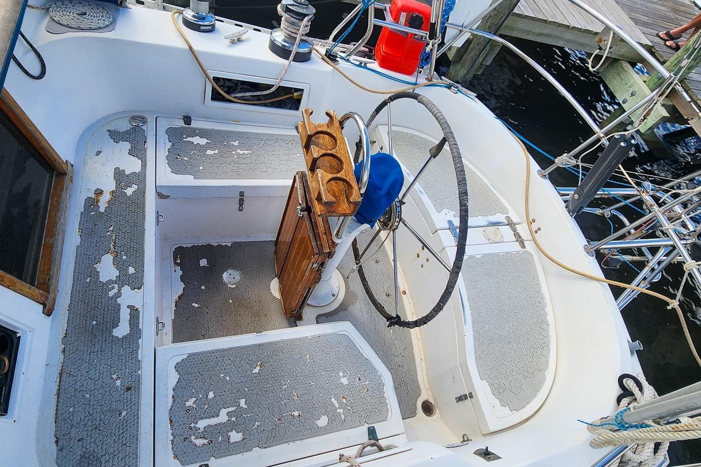 Cockpit of a 1980 Nordic 44 sailboat with weathered flooring and steering wheel.