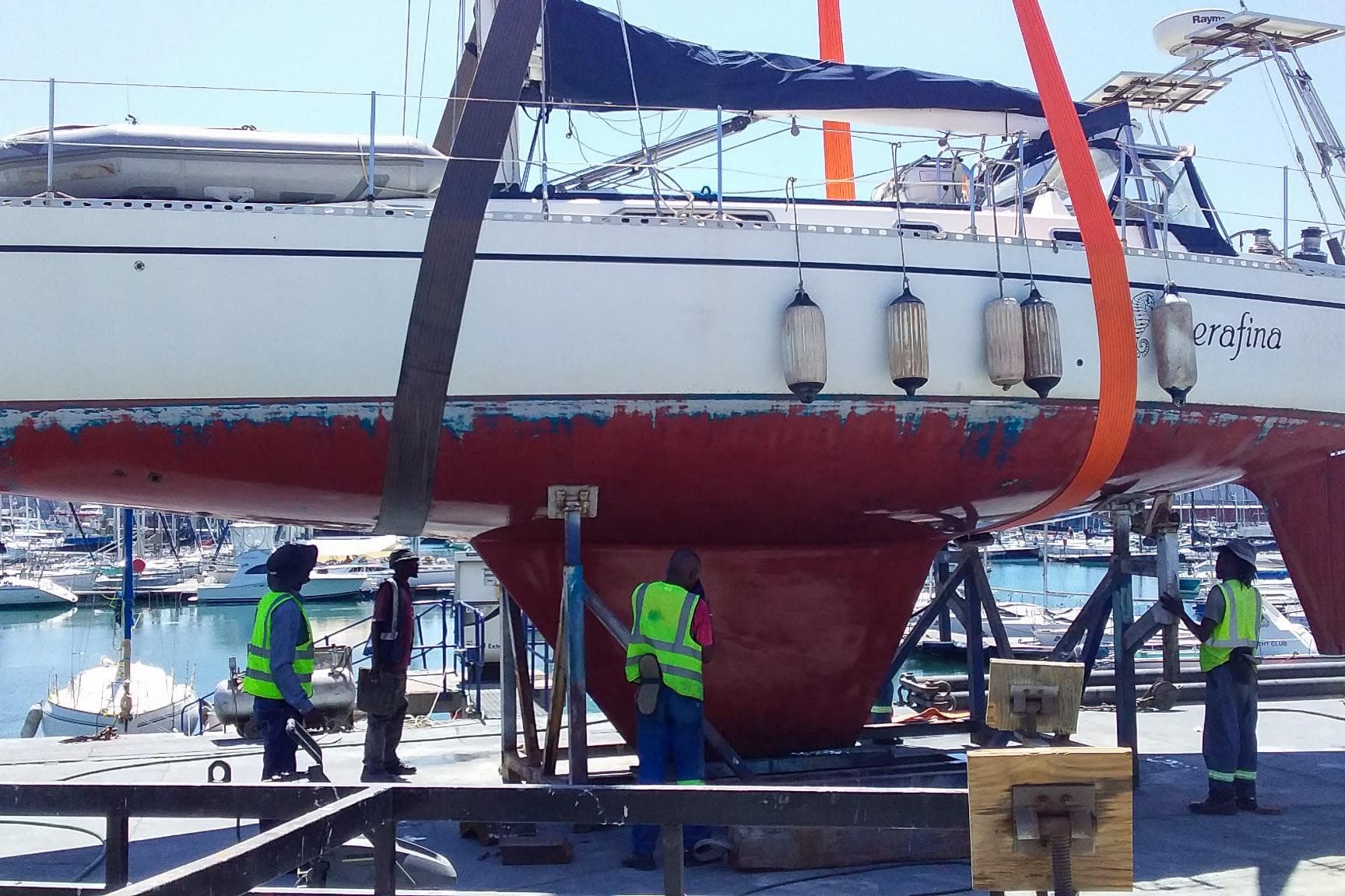Nordic 44 sailboat from 1980 being lifted at a marina with workers in safety vests.