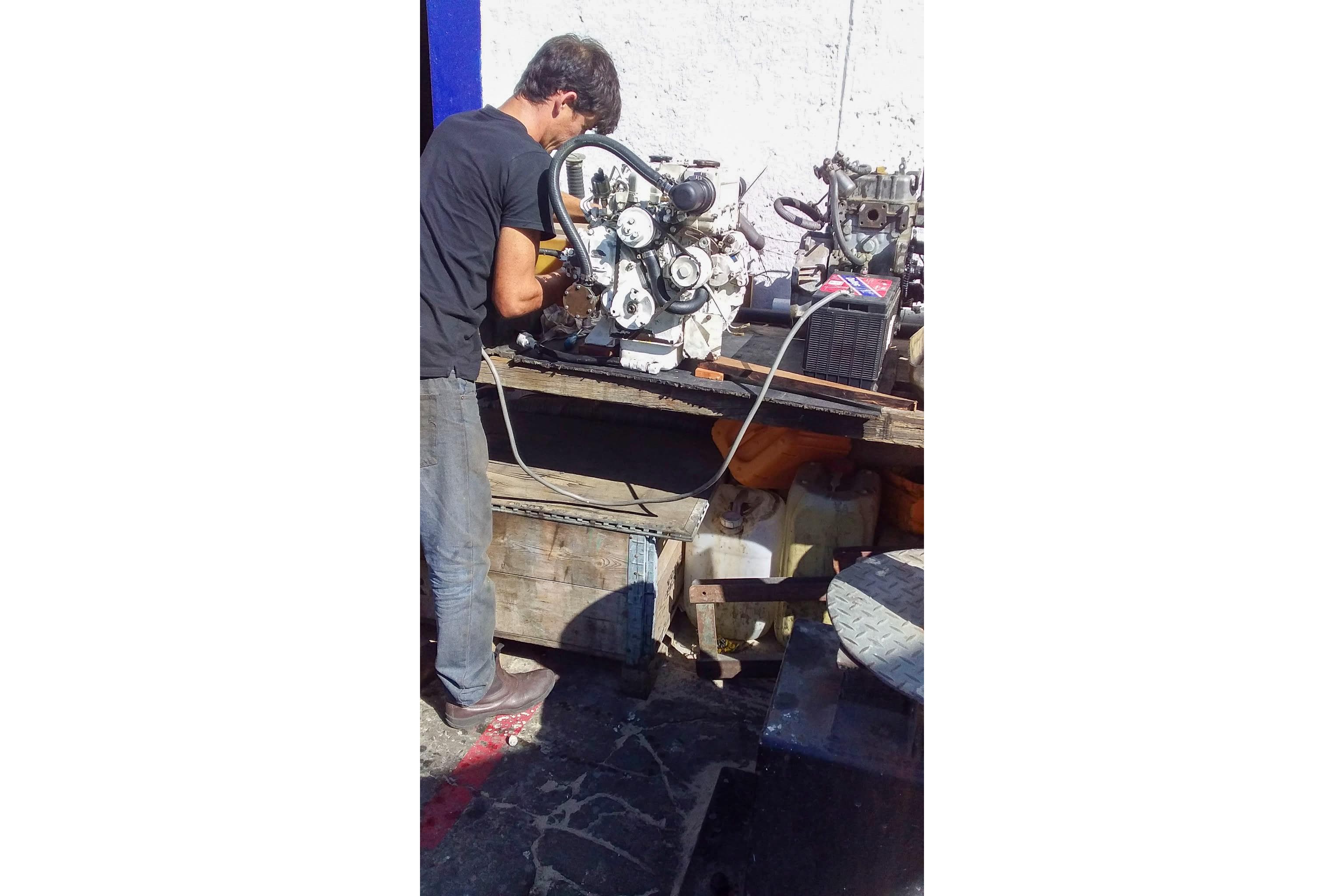 Man repairing Nordic 44 engine, 1980 model, outdoors on a sunny day.
