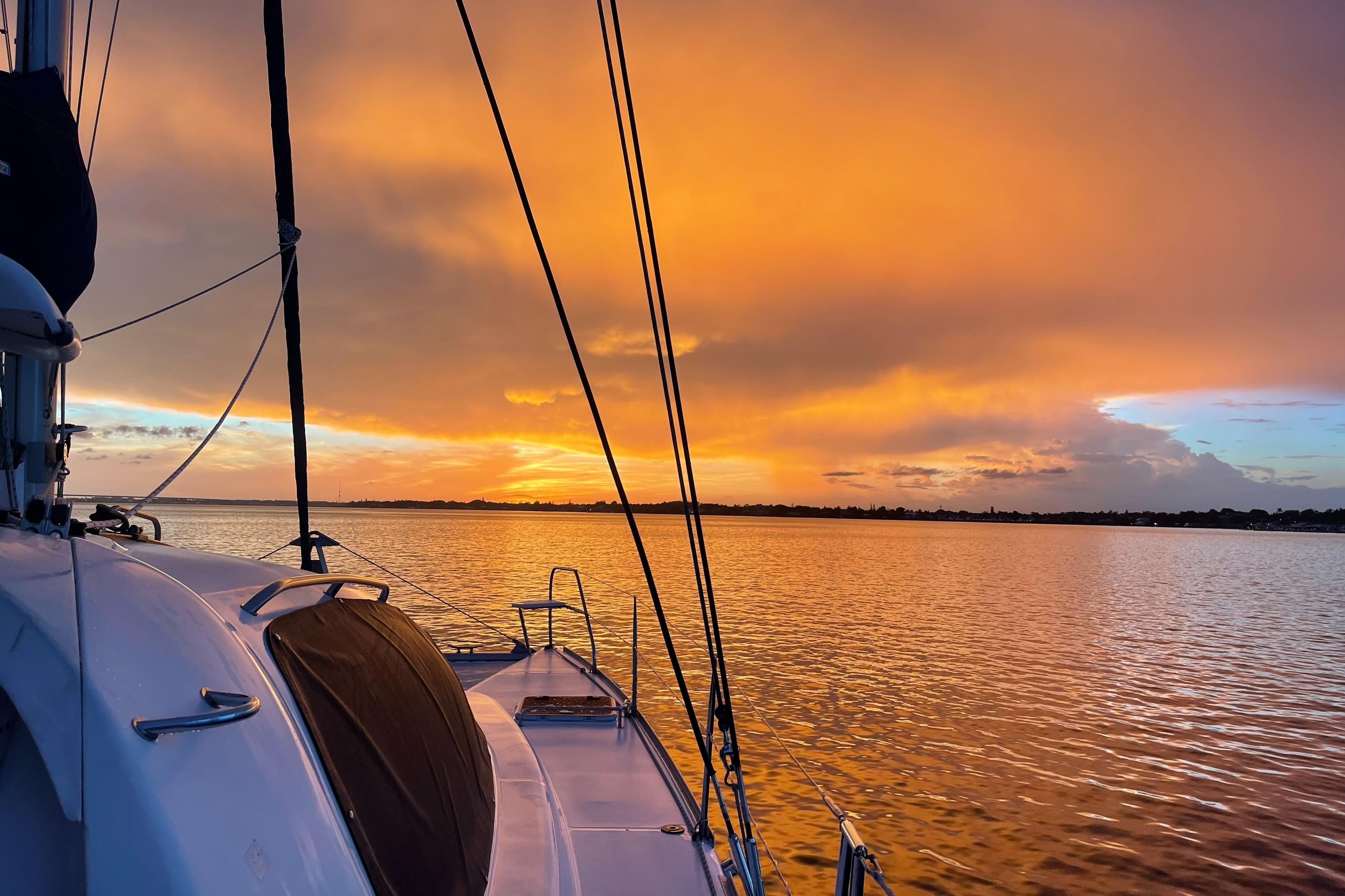 Leopard 40 catamaran sailing at sunset, vibrant orange sky reflecting on calm water.