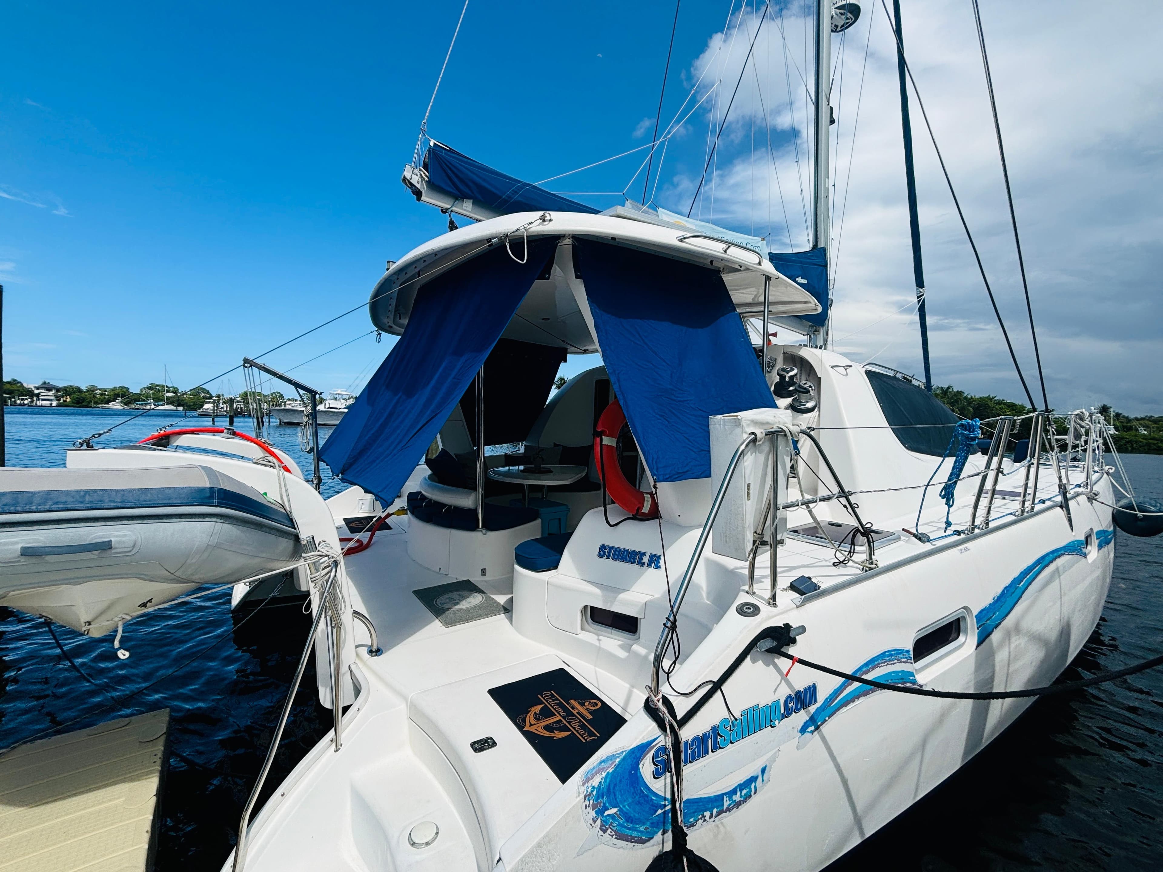 2006 Leopard 40 catamaran docked, featuring blue accents and a dinghy, under a clear sky.